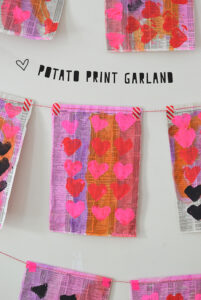 Kids make heart printed garland with potatoes, paint, and newspaper.