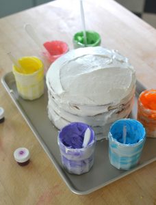 Kids collaborate to paint a cake using colored frosting.
