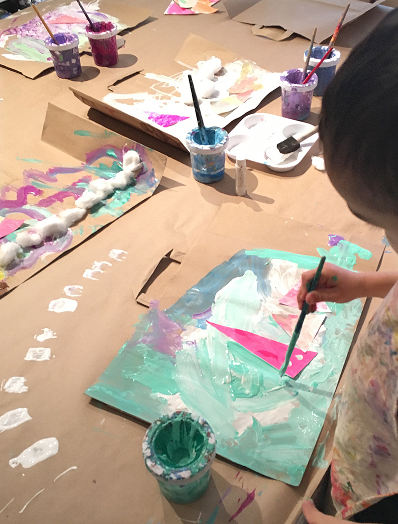 Children create mixed-media collage paintings on recycled paper bags.