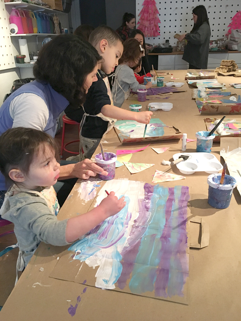 Children create mixed-media collage paintings on recycled paper bags.