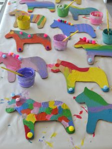 Children paint cardboard dala horses at a birthday party.