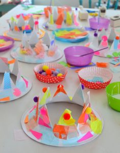 Kids make party hats from paper plates and collage material.