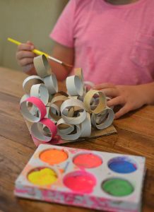 Children use cut up pieces of toilet paper tubes to build sculptures with glue.
