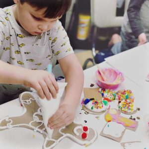 Kids use homemade puffy paint to decorate giant cardboard gingerbread men and cardboard gingerbread houses.