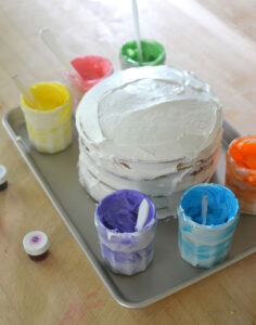 Kids decorate a birthday cake together with a paint palette of different colored frostings.