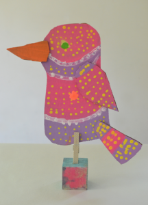 Kids make cardboard birds and attach them to wooden blocks for display.