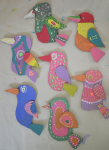Kids make cardboard birds and attach them to wooden blocks for display.