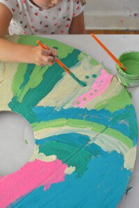 Mixing paint colors using tempera paints to paint giant cardboard donuts.