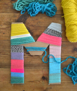 Kids wrap cardboard letters with yarn.