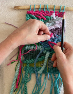 Tucking the ends into the back of a colorful doodle weaving, made with a cardboard loom