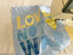 Sewing on fabric letters to "Love Not War" DIY banner made with old shirts.