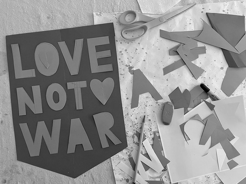 Cutting letters from paper as templates to make "Love not War" banners from old shirts.