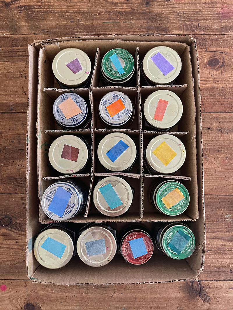 Jars of hand-mixed liquid watercolor in a cardboard storage box.