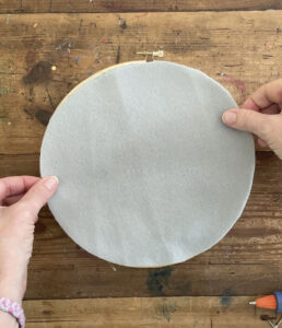Gluing on a piece of felt to the back of an embroidery hoop used to make a round weaving