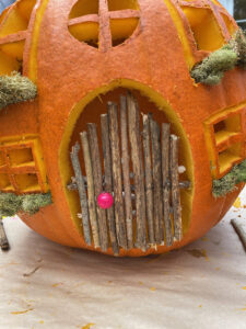 Securing the twig door onto the pumpkin cottage with a glue gun