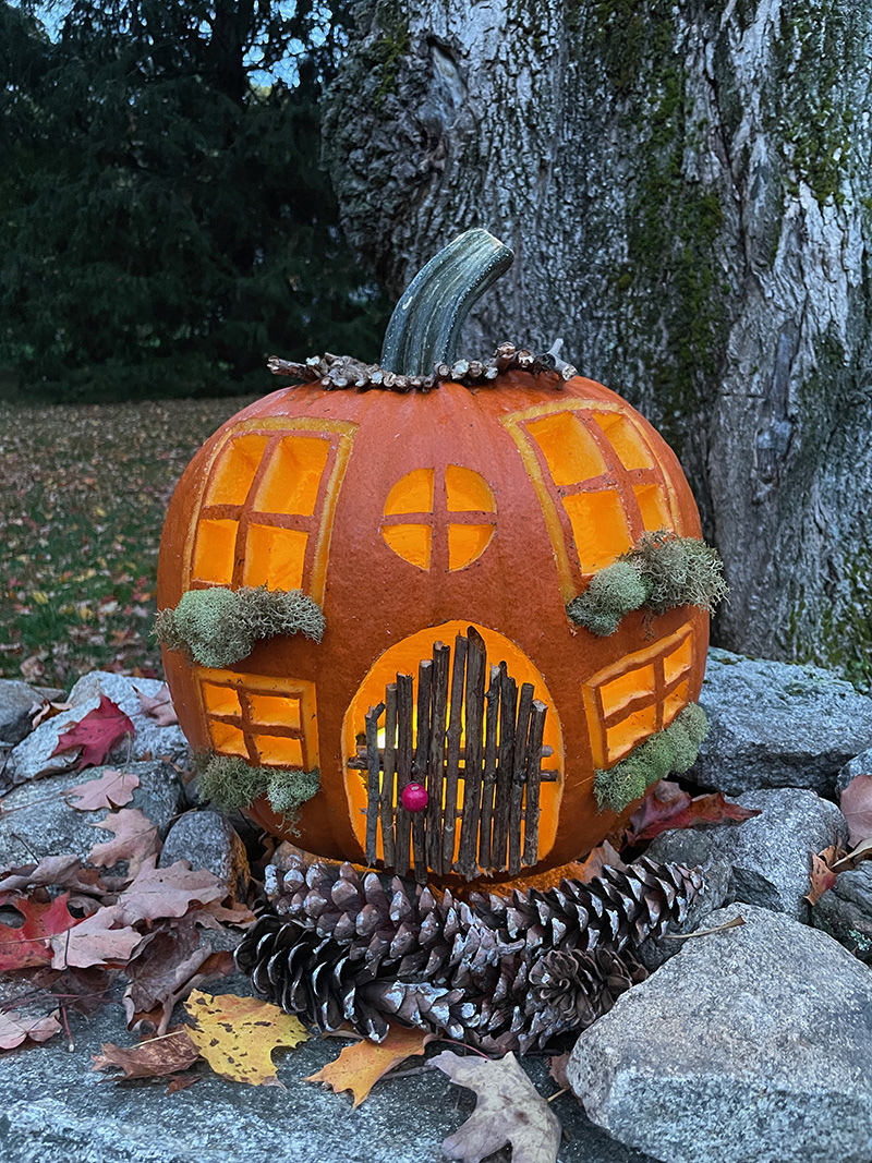 Carved pumpkin cottage on a wall at dusk, lit from the inside