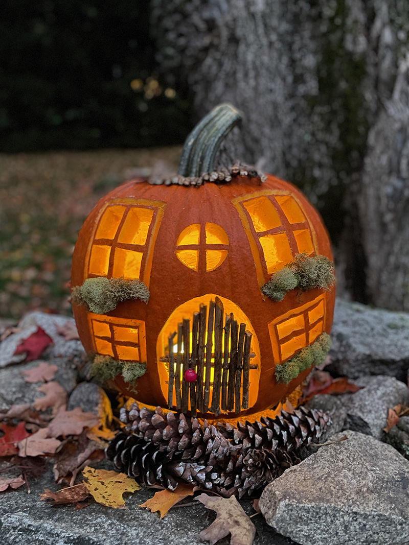 Carved pumpkin cottage on a wall at night, lit from the inside
