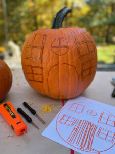drawing out the details of the pumpkin cottage on the pumpkin before cutting