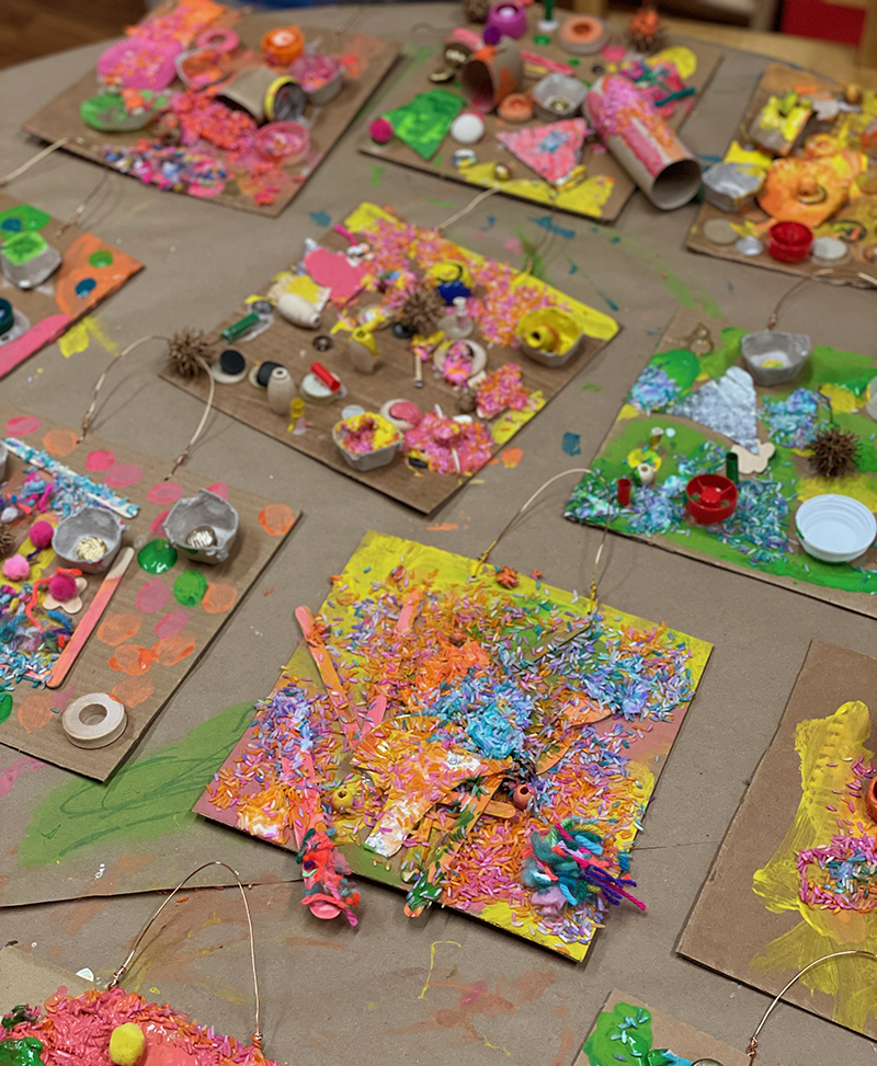 A whole table of colorful, recycled collages made by preschoolers.