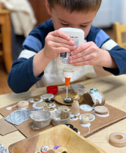 Preschooler using glue to make a recycled collage using 3-dimensional materials.