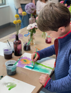 Young boy is painting with liquid watercolor at the flower still-life table.