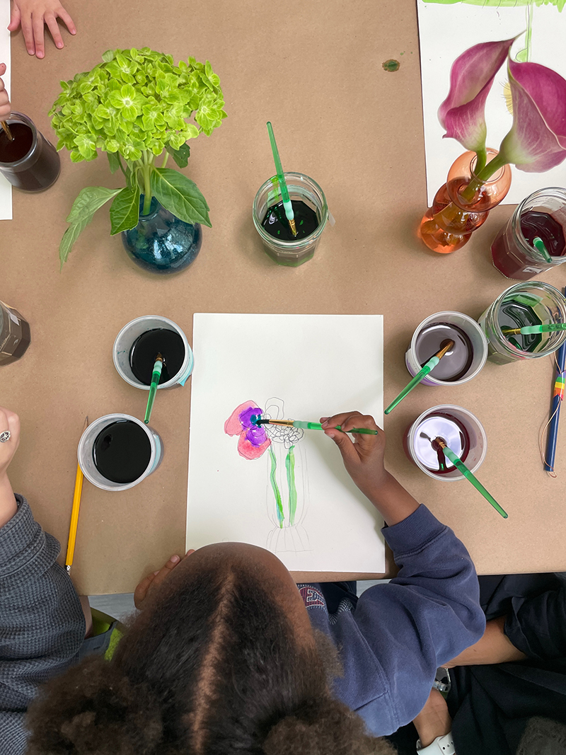 Child observes a flower vase in front of her and paints what she sees.