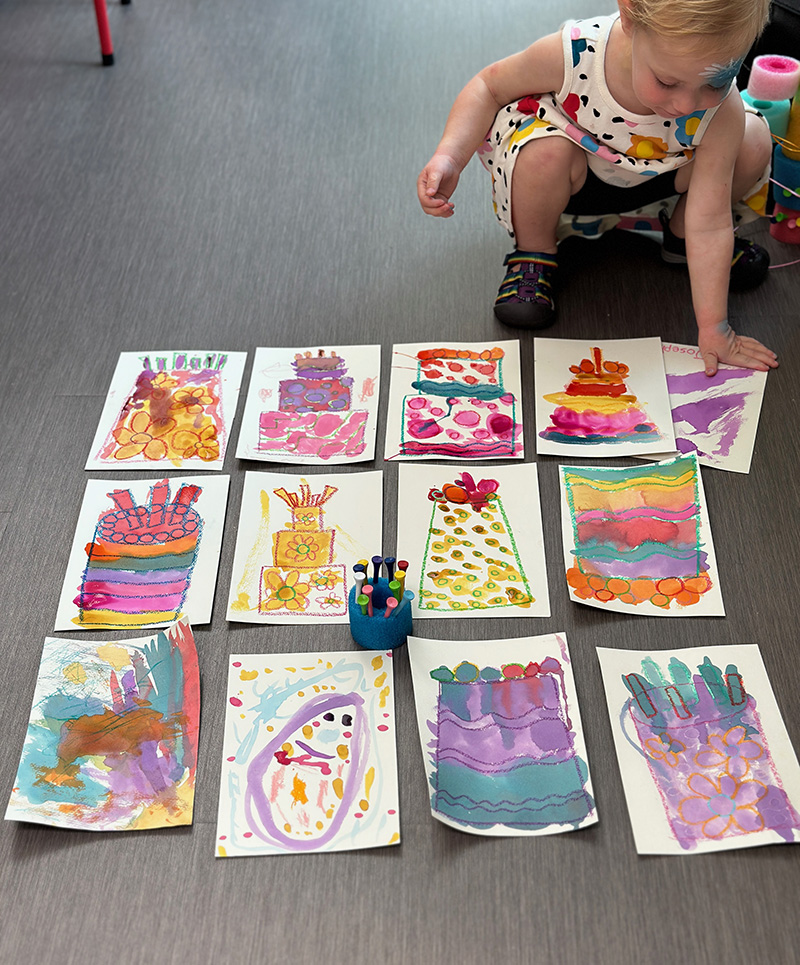 Young child lays out a collection of cake paintings on the floor.