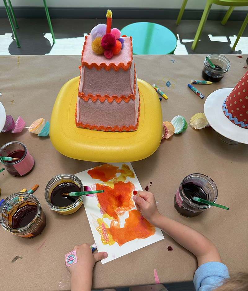Child using liquid watercolor and oil pastels to paint a cake from a still life.