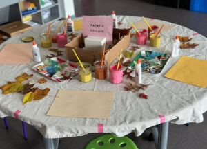 Table set up and ready for mixed-media collage with leaves, fabric scraps, tempera paint, and colored construction paper.