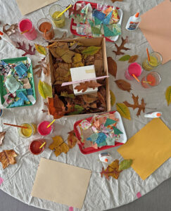 Table set up and ready for mixed-media collage with leaves, fabric scraps, tempera paint, and colored construction paper.