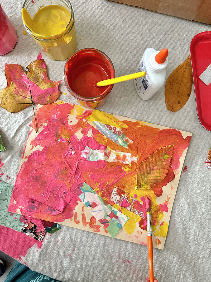 Child paints with tempera paints on top of her leaf and fabric collage.
