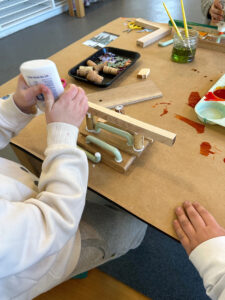 Children build and create with wood, liquid watercolor, collage, and glue.