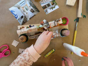 Overhead view of a child building and creating with wood, liquid watercolor, collage, and glue.