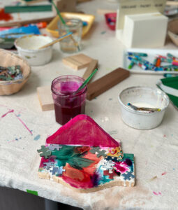 Painted wood structure with glued puzzle pieces on a table with other materials.