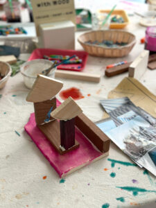 Wood structure made by a child using liquid watercolor on a table with other materials like magazine clippings and oil pastels.