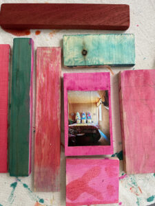Painted wood pieces, on that has a magazine clipping glued on top, lying on a table.
