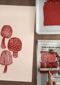 Red printing ink is rolled on top of one of 4 different mushrooms made from styrofoam to create a patterned print.