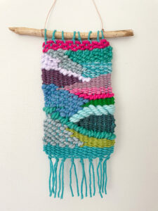 A colorful doodle weaving hanging up with a stick and some wire, a small size perfect for children to make.