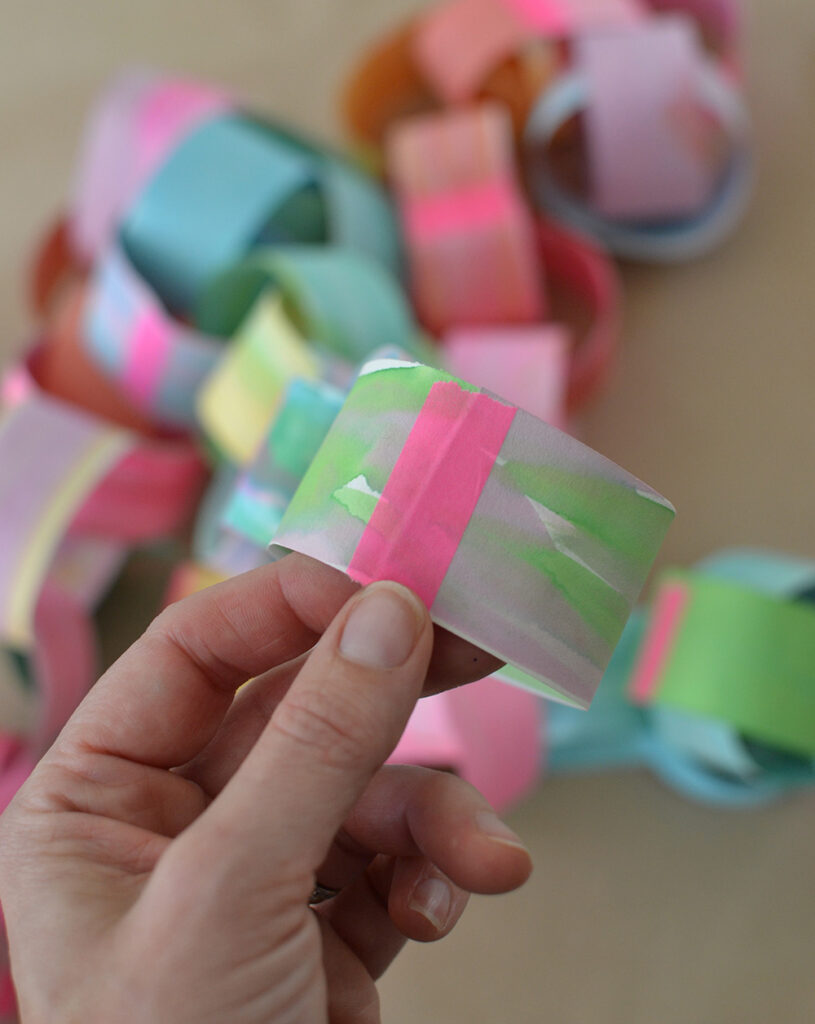 Make a colorful, rainbow paper chain using hand painted paper and neon tape.
